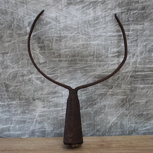 May include: A rusty, antique garden tool with a curved, U-shaped top and a long, tapered handle. The metal tool has a weathered appearance, suggesting age and use. The tool is likely used for gardening or farming tasks.