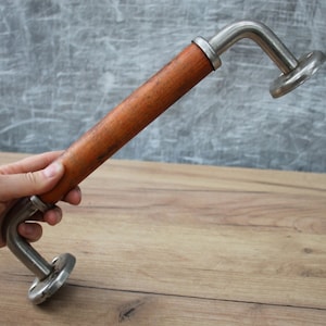 Może przedstawiać: Srebrny i drewniany klamka do drzwi o zakrzywionym kształcie. Klamka jest wykonana z metalu i ma drewniany uchwyt. Klamka jest przymocowana do metalowej płytki.