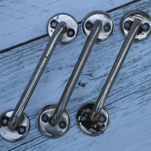 May include: Three silver metal cabinet door handles with rounded edges and two holes for screws. The handles are arranged in a staggered pattern.