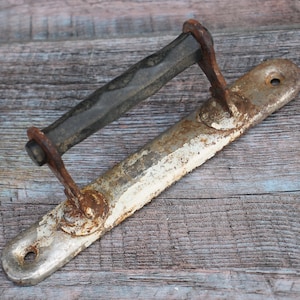May include: A vintage, white-painted metal door handle with a black metal bar. The handle has a rusty patina and is attached to a wooden surface.