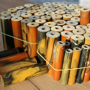 Peut inclure: Ensemble de pièces cylindriques en bois aux tons marron, jaune et noir, maintenues par des élastiques verts. Chaque pièce est percée d'un trou central. Le veinage du bois crée un effet marbré. Mesures en centimètres.