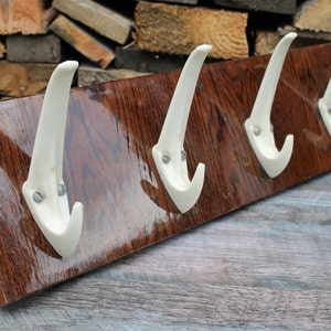 Puede incluir: Un perchero de madera con cuatro ganchos de cerámica blanca. El perchero tiene un acabado de madera de grano marrón oscuro.