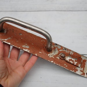 May include: A vintage metal door handle with a silver finish and a rusty brown patina. The handle is rectangular with a curved metal bar for pulling.