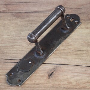 May include: A vintage, rusty metal door handle with a long, rectangular backplate and a rounded handle. The handle has a keyhole and a small, diamond-shaped plate on the backplate.