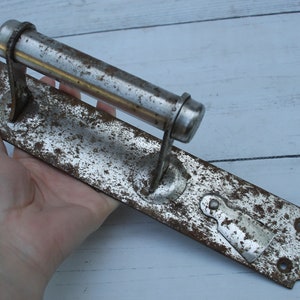 May include: A vintage, silver-toned door handle with a long, cylindrical lever. The handle is rusty and shows signs of wear and tear.