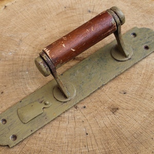May include: A vintage door handle with a wooden knob and a metal plate. The handle is painted in a muted green color and has a distressed look.