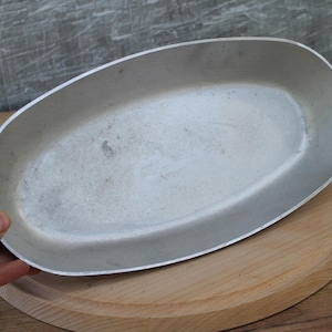 May include: A silver oval baking dish with a smooth, shiny surface. The dish is empty and appears to be made of aluminum.