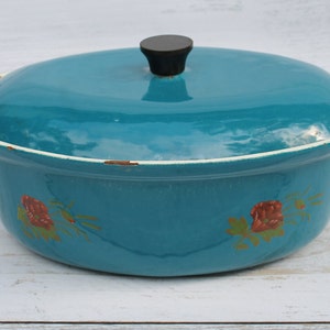 May include: Teal enamel cast iron casserole dish with a lid and white handles. The dish has a floral design with red roses.