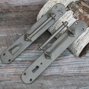 May include: Two antique metal door handles with a dark green finish. Each handle has a metal rod and a keyhole. The handles are on a wooden surface.