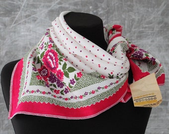 Pode incluir: Um lenço branco com uma borda rosa e um padrão floral. O lenço está dobrado e exibido em um manequim preto. O lenço tem um padrão de bolinhas brancas no centro.