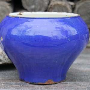 May include: A large, blue ceramic pot with a white rim. The pot has a rounded, bulbous shape and a slightly flared lip.