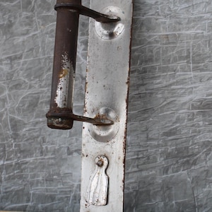 Peut inclure: Une poignée de porte vintage avec une finition argentée et un levier en métal rouillé. La poignée a un trou de serrure et des détails décoratifs.