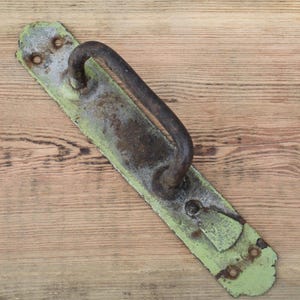 Peut inclure: Une poignée de porte ancienne avec une poignée incurvée. La poignée est montée sur une plaque rectangulaire avec une finition de peinture verte délavée et vieillie. Le métal montre des signes d'âge et d'usure, avec de la rouille et une décoloration.