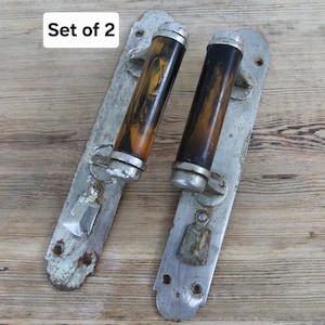 May include: A set of two door handles featuring long, silver-toned metal backplates with visible screw holes and weathered surfaces. Each handle has a cylindrical grip with a marbled brown and black pattern and silver-toned metal end caps.