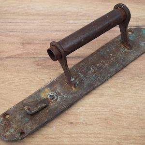 May include: A rusty metal door handle with a long, cylindrical handle and a rectangular plate. The handle has a patina of green and brown rust.