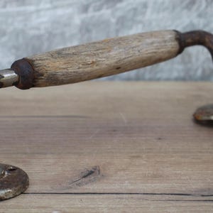 May include: An antique door handle with a wooden grip and aged metal hardware. The handle features a curved design with a cylindrical wooden grip and two circular mounting plates. The metal shows signs of rust, giving it a vintage appearance.