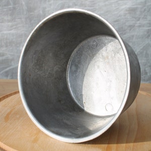 May include: A silver aluminum pot with a smooth, slightly textured surface. The pot is empty and has a rounded bottom.