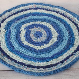 Könnte beinhalten: Ein runder, blau-weißer geflochtener Teppich mit einem konzentrischen Kreisdesign. Der Teppich ist aus recycelten Stoffresten gefertigt und hat einen rustikalen, handgefertigten Look.