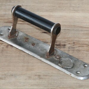 May include: An antique door handle with a black cylindrical grip and a rectangular, aged metal base. The base has a distressed finish with visible rust and mounting holes, suggesting vintage hardware.