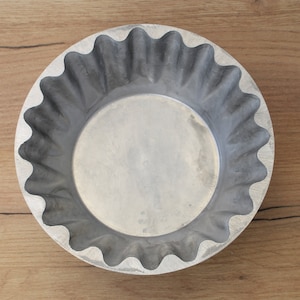 May include: A silver metal pie pan with a fluted edge. The pan is empty and has a smooth, shiny surface.