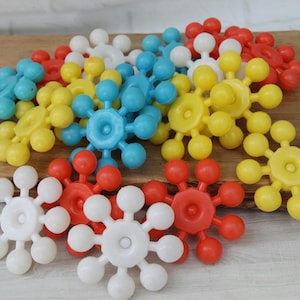 May include: A collection of plastic snowflake-shaped building blocks in bright red, yellow, blue, and white colors. Each piece features a central hexagonal hub with eight radiating spokes ending in small spheres, designed for interlocking assembly.