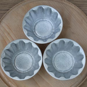 Może przedstawiać: Trzy srebrne metalowe formy do pieczenia z karbowanymi krawędziami. Formy są ułożone w kształt trójkąta na drewnianej powierzchni.