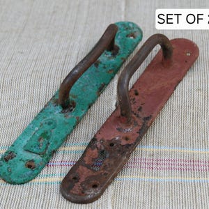 May include: Set of two vintage door handles. One is painted green, the other is red. Both have a curved handle and a rectangular base with visible wear and tear, suggesting age and use. The text "SET OF 2" is in the top right corner.