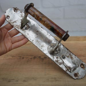 May include: An antique, weathered metal toilet paper holder. The holder features a long, rectangular backplate with mounting holes and a decorative end. The roller is made of a dark, patterned material.