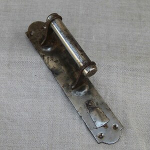 May include: A vintage metal door handle with a rectangular backplate and a cylindrical handle. The handle and backplate have a distressed, aged appearance with signs of wear and rust. The hardware is likely for a door or cabinet.