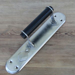May include: A silver-toned metal door handle featuring a cylindrical black grip mounted on an elongated rectangular backplate with rounded ends. The backplate includes four pre-drilled screw holes and a decorative diamond-shaped metal accent.