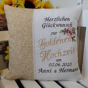 May include: White pillow with gold embroidery that says "Herzlichen Glückwunsch zur Goldenen Hochzeit am 02.06.2023 Anni & Hermann" with a pink rose graphic. The pillow has a beige background with a white swirl pattern.