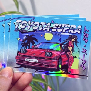 以下が含まれることがあります： 赤いトヨタスープラと、ピンクと白の服を着た女性が隣に立っているステッカー。ステッカーは、青、ピンク、黄色のカラーリングで、レトロな80年代の雰囲気。"TOYOTA SUPRA"の文字は、太字の白で書かれている。