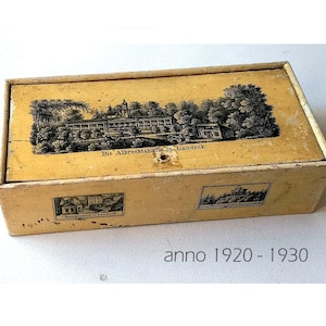 Könnte beinhalten: Eine vintage gelbe Schachtel aus Pappe mit Schwarzweißillustrationen eines Gebäudes und dem Text "Die Albrechtstalle in Landeck". Die Schachtel hat auf jeder Seite ein kleines Bild eines Gebäudes.