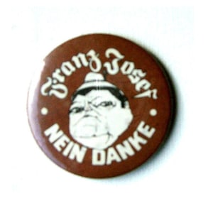 Könnte beinhalten: Ein brauner Knopf mit einem weißen Cartoon-Bild eines Mannes mit Hut und dem Text "Franz Josef Nein Danke".