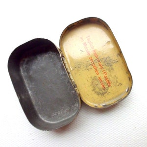 May include: A yellow metal tin with a red and black label that reads "T&auml;glich mehrmals 1 Pastille im Munde zergehen lassen". The tin is open and the inside is empty.