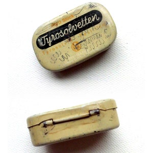 May include: A vintage metal tin with a hinged lid. The tin is cream colored with black lettering that reads "Tyrosolvetten 20 Stuck".