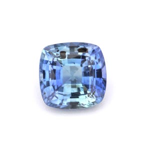May include: A square-cut, faceted gemstone with a gradient of blue hues. The gem transitions from a deep indigo at the edges to a lighter, almost translucent blue in the center. The facets create a play of light and shadow.