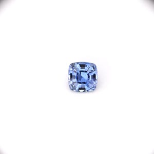 May include: A square-cut, light blue gemstone with a faceted surface. The gem is set against a white background, showcasing its clarity and color. The gemstone's facets reflect light, creating a sparkling effect.