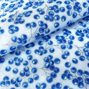 Könnte beinhalten: Nahaufnahme eines Stoffes mit einem sich wiederholenden Muster aus blauen Beeren und grauen Stielen auf weißem Hintergrund. Der Stoff ist gefaltet und zeigt die Details des Musters. Die Beeren haben ein glänzendes Aussehen.