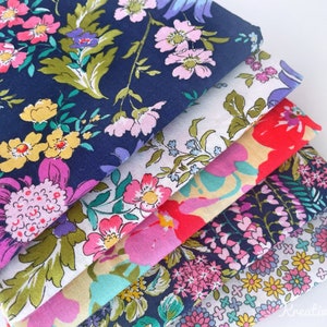 Könnte beinhalten: Ein Stapel Stoffmuster mit Blumenmustern in verschiedenen Farben. Die Stoffe zeigen Muster aus rosa, gelben und lila Blumen mit grünen Blättern auf marineblauen, weißen und roten Hintergründen. Die Stoffe sind ordentlich gefaltet und gestapelt.