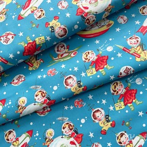 May include: A blue fabric featuring a retro space-themed pattern. The design includes cartoon astronauts, rockets, planets, and stars. The astronauts are depicted in yellow and red space suits, with a vintage aesthetic.