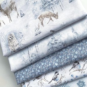 May include: A stack of winter-themed fabric featuring various designs. The top fabric displays deer, an owl, and snowflakes in a snowy forest scene. Other fabrics showcase berry patterns, birds on branches, and snowflake motifs in shades of blue and white.