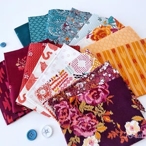 Può includere: Una collezione di quadrati di tessuto colorati con vari motivi e stampe, tra cui floreali, geometrici e astratti. I tessuti sono disposti a ventaglio, con bottoni blu sparsi.