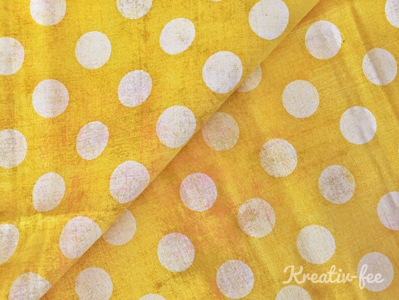 Peut inclure: Tissu jaune vif orn&eacute; de grands pois blancs. Le tissu est pli&eacute;, r&eacute;v&eacute;lant la texture et les variations de couleur. L'image a un aspect vintage ou vieilli.