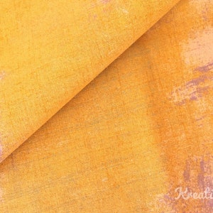 Peut inclure: Gros plan sur un tissu textur&eacute; aux tons jaune et orange avec de subtils coups de pinceau violets. Le tissu a un aspect l&eacute;g&egrave;rement pli&eacute;, r&eacute;v&eacute;lant sa texture en couches. L'esth&eacute;tique g&eacute;n&eacute;rale sugg&egrave;re un design rustique ou abstrait.