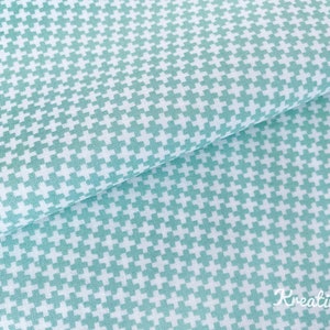 Può includere: Primo piano di un tessuto piegato con un motivo ripetuto di piccoli segni più turchese chiaro su sfondo bianco. Il tessuto ha un aspetto morbido e strutturato, adatto a vari progetti di cucito.