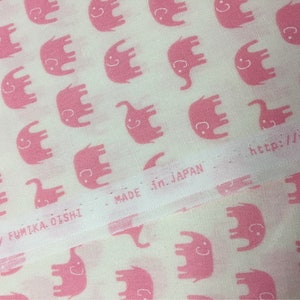 Puede incluir: Tela blanca con un patr&oacute;n repetido de elefantes rosas con caras sonrientes. El texto "MADE in JAPAN" es visible. La tela es producida por FUMIKA OISHI. La direcci&oacute;n del sitio web tambi&eacute;n es visible.