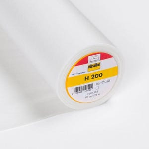 May include: A roll of white interfacing fabric, labeled "H 200" with dimensions of 90 cm x 25 m. The label features red, yellow, and white colors. The fabric is made of 100% PES.