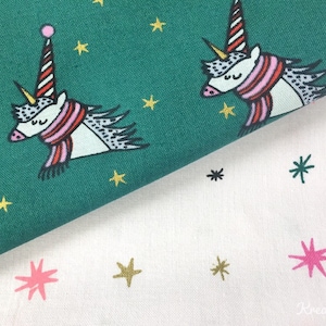 Könnte beinhalten: Grüner Stoff mit einem sich wiederholenden Muster aus skurrilen Einhörnern mit gestreiften Hüten und Schals, umgeben von goldenen Sternen. Der Stoff ist über einem weißen Stoff mit rosa Sternen und dem Text "Kreativfee" gefaltet.