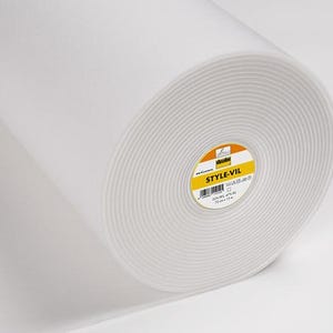Könnte beinhalten: Eine große Rolle weißen Style-Vil-Vliesstoffs. Der Stoff ist eng gewickelt und zeigt konzentrische Kreise. Ein gelb-oranges Etikett mit dem Text "STYLE-VIL" ist sichtbar. Der Stoff ist 183 cm breit.